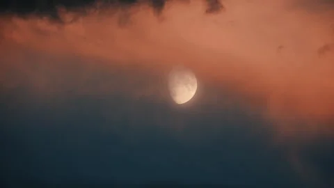 The moon behind moving orange sunset clouds in the blue sky Stock Footage 344983037