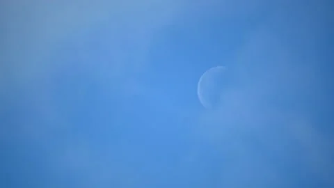 The moon can be seen in the blue sky on bright day and light clouds pass by Stock Footage 130450028