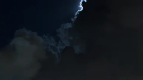 Moon fights billowing clouds at night against deep blue sky timelapse Stock Footage 108393321