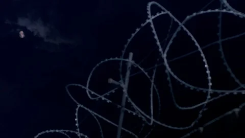 The moon hides behind heavy clouds over the barbed wire. Stock Footage 115333272