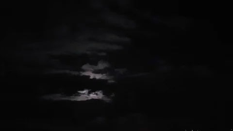 The moon in the night sky comes out from behind the clouds. Timelapse. Stock Footage 88992566