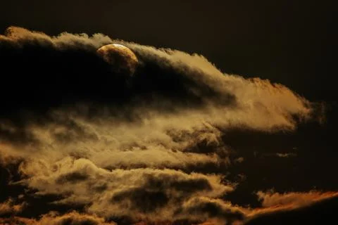 Moon partially obscured by dark clouds during twilight, illuminated by soft.. Stock Photos