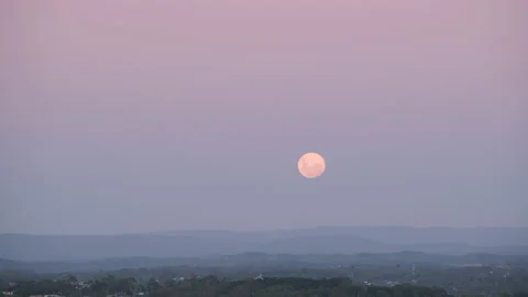 The moon rises over mountains during dusk Stock Footage 232766004