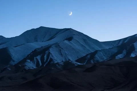 The moon rises over the snow-capped mountains in the evening after the sun ha Stock Photos