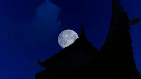 The moon rises past the eaves of ancient buildings at night Stock Footage 240154647