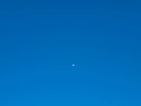 The moon rises when it is still day and the sky is clear blue Stock Photos