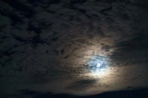 Moon shining through clouds at night with textured cloud cover Stock Photos