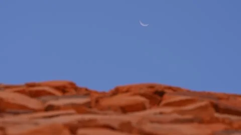 Moon slice in blue sky with desert landscape blurred in foreground. Static Stock Footage 288437403