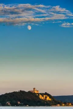 Moon under scattered clouds over a castle on a lake at sunset Stock Photos