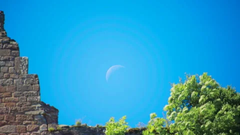 Moon visible in clear blue sky above historic castle ruins Видео 327568933