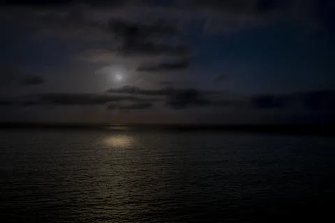 Moonlight illuminates the dark ocean waves under a cloudy night sky 库存照片