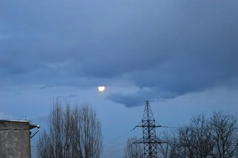 Moonlight peeking through clouds over a tranquil landscape with power lines Stock Photos