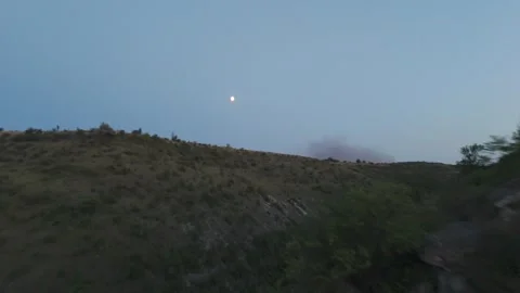 Moonlit landscape over rolling hills with sparse vegetation and a distant plume Stock Footage 332725643
