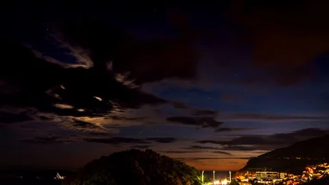 Moonset through the clouds over sea. Night moon setting over a small city. Video stock 91896505