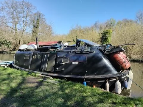 A moored dark-colored narrowboat along a canal bank Stock Photos