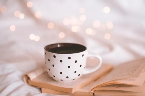 Morning cup of black tea with stack of open paper books in bed close up. Good Foto stock
