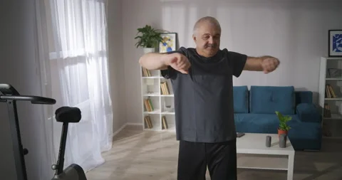Morning exercise of middle aged man in living room, person is stretching arms Видео 146768007