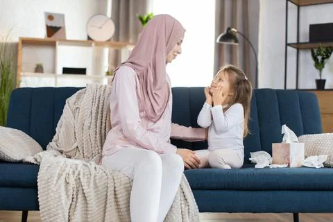 Morning higiene routine at home. Happy Muslim mom in hijab, sits on sofa at cozy Stock Photos
