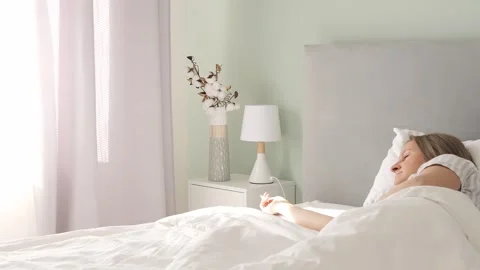 Morning light streams through the window casting onto sleeping woman in bedroom Stock Footage 274136147