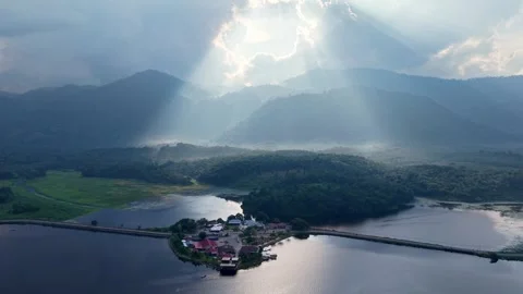 Morning sun rays breaking through clouds over serene lake and mountainous Stock Footage 339824710