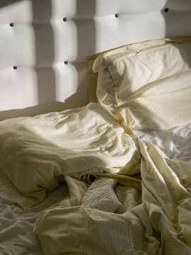 Morning sunlight and soft shadows falling across an unmade bed Stock Photos