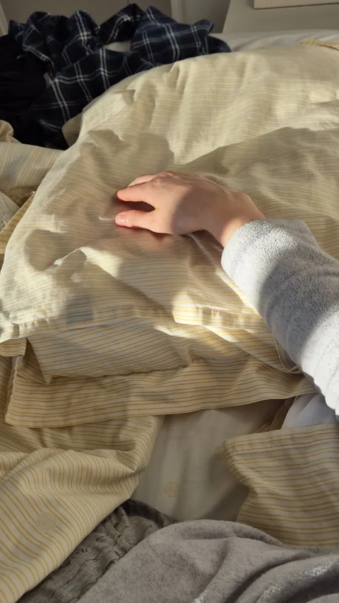 Morning sunlight casting soft shadows over a rumpled bed as a relaxed hand rests Stock Footage 331006662