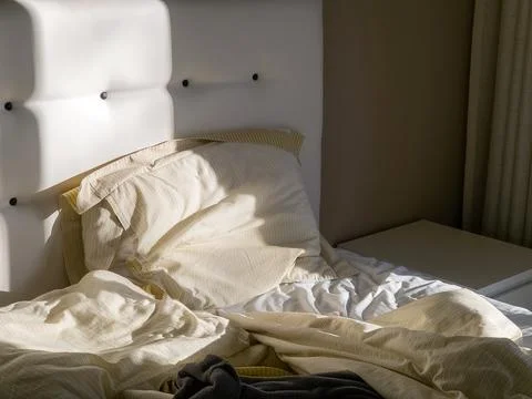 Morning sunlight casting soft shadows across an unmade bed Stock Photos