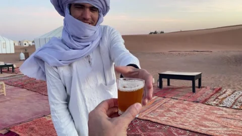 Moroccan man serves hot mint tea at a luxury outdoor camp in Sahara Desert Stock Footage 276228480