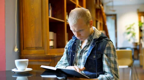 Morose student sitting in the library and looking for something in the book Stock-Footage 67541750