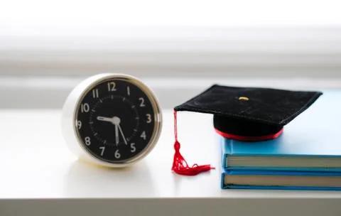 Mortarboard and alarm clock on stack of books, isolated in white background Stock Photos