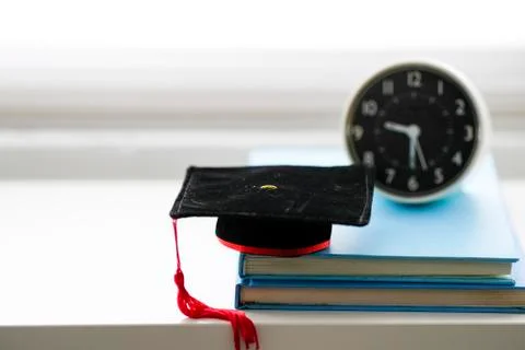 Mortarboard and alarm clock on stack of books, isolated in white background Stockfoto's