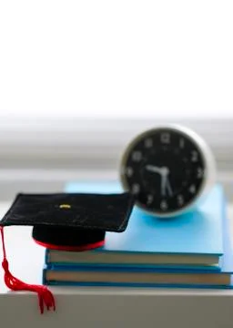 Mortarboard and alarm clock on stack of books, isolated in white background Stockfoto's
