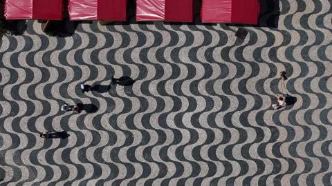 Mosaic pattern of wavy cobblestones with people walking beneath red canopies Stock Footage 316689389