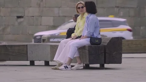 Moscow, Russia - May 18, 2026: Two Friends Sitting on a City Bench Chatting in C Video stock 338390853