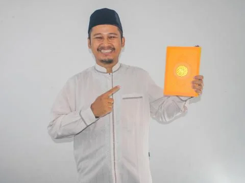 Moslem Asian man smiling while pointing to a book that he hold Stock Photos