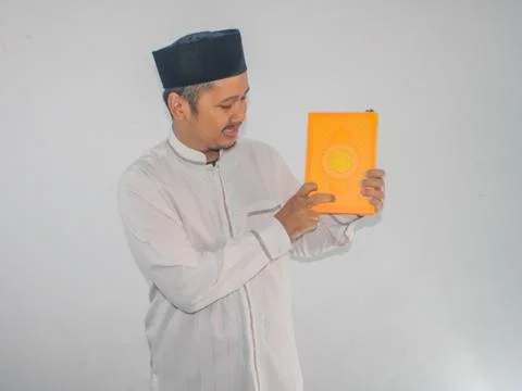 Moslem Asian man smiling while pointing to a book that he hold Stock Photos
