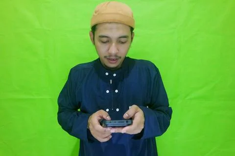 Moslem Asian man texting using his mobile phone isolated on green background Stock Photos