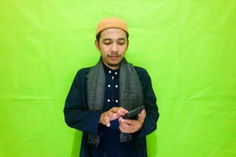 Moslem Asian man texting using his mobile phone isolated on green background Stock Photos