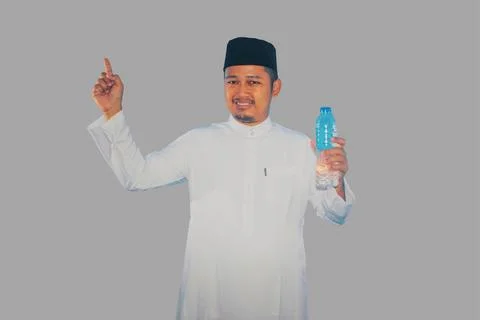 Moslem man smiling while holding a bottle of drinking water and pointing to.. Stock Photos