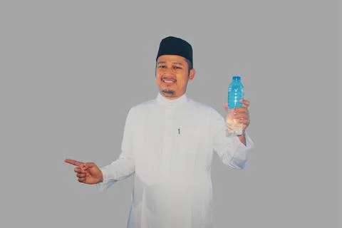 Moslem man smiling while holding a bottle of drinking water and pointing to.. Stock Photos