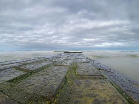 Moss-Covered Jetty Extending Into The Wave-Washed Ocean Under Cloudy Skies Stock Photos