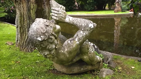 Mossy Old Sculpture of a Man Drinking in a Botanical Garden 库存影片 336652333