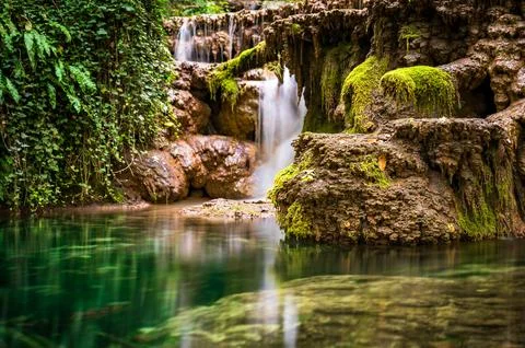 Mossy waterfall cascading into clear emerald pool travertine Stock Photos