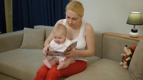 Mother 40 years old reading a book a small child sitting on the couch Stock Footage 69958748