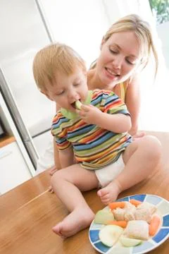 Mother and baby in kitchen eating fruit and vegetables Stock Photos