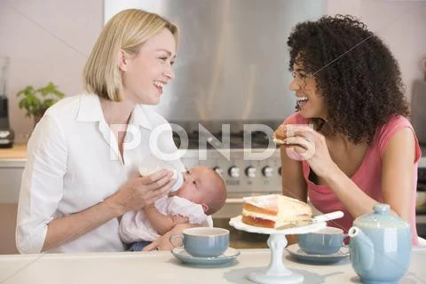 Mother and baby in kitchen with friend eating cake and smiling Stock-Fotos