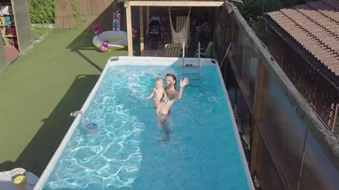 A mother and a baby in a pool. Elevating drone shot showing whole neighborhood Stock Footage 138313960