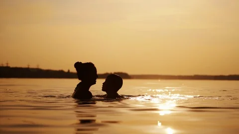 Mother and boy inside the river water at sunset. Silhouette of a woman throwing Stock Footage 114649505
