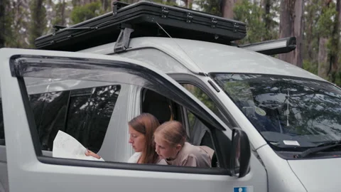 Mother and child explore a map while parked in a van among tall trees Video stock 318475223