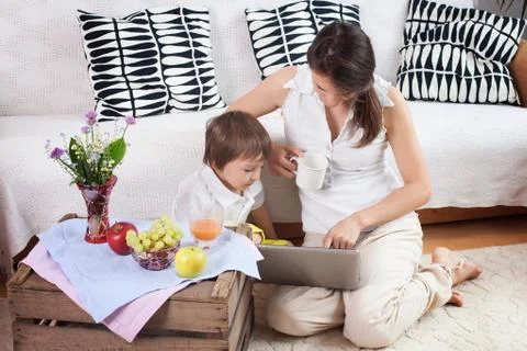 Mother and child, looking at a computer, eating fruits at cozy home Stock Photos